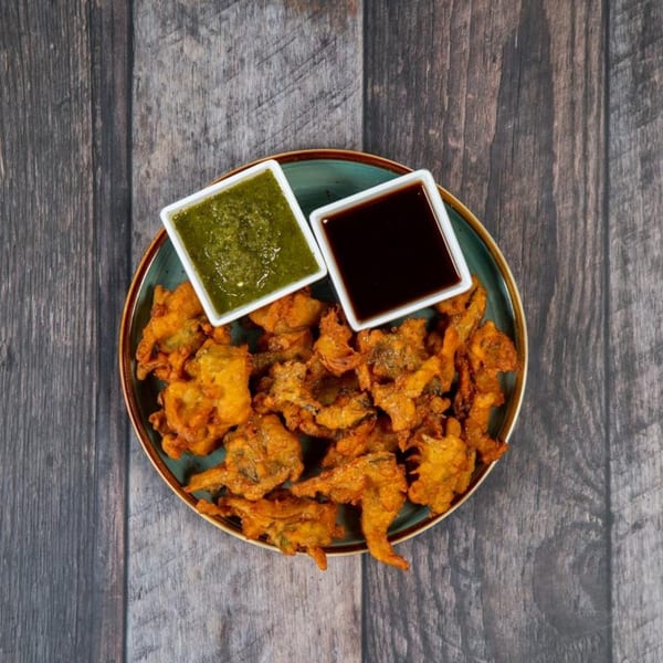 A plate of golden-brown pakoras with two dipping sauces, one green and one dark brown.