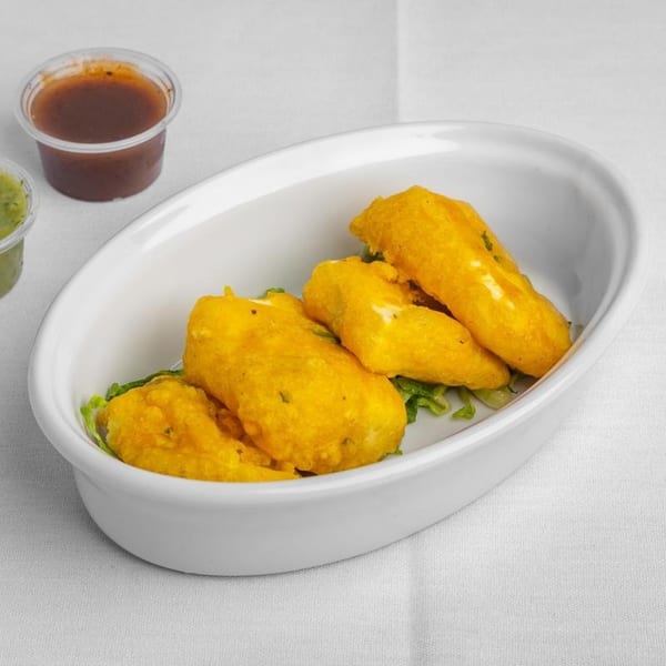 Golden-fried paneer pakora on lettuce in a white dish, with two small sauce cups.