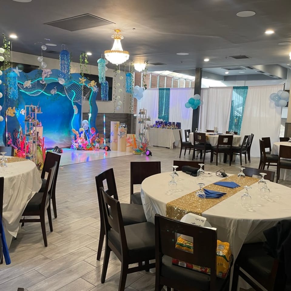 Festive restaurant event space with round tables, gold runners, and an 'under the sea' themed stage.