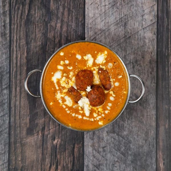 Overhead view of a metal bowl filled with orange curry, meatballs, and white cheese crumbles.