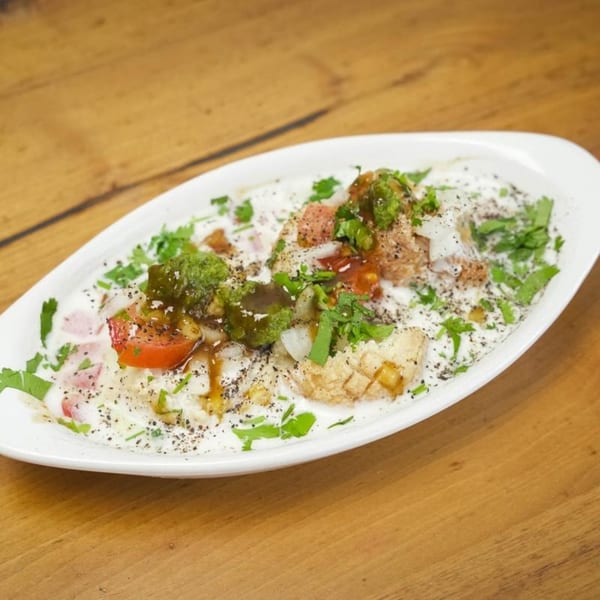 Dahi Bhalla, a savory Indian dish, topped with yogurt, chutneys, spices, and fresh herbs.