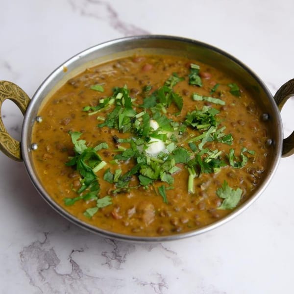 A metal bowl of creamy Dal Makhani, garnished with fresh cilantro and a dollop of butter.